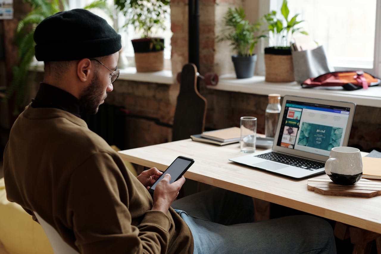 Male designer working on laptop and phone in a modern home office setting.